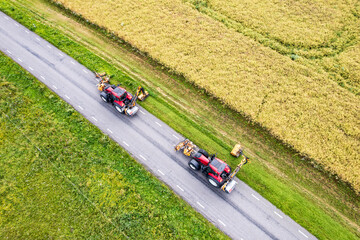 Drone view of two tractors with a mechanical mowers mowing grass on the side of the asphalt road