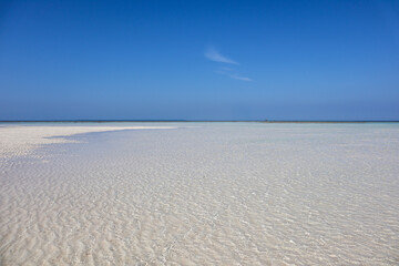 A wide beach view with calm shallow waters and a wide, flat expanse of pale sand