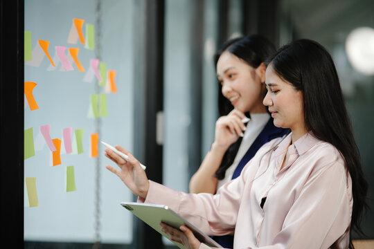 Two businesswomen standing with sticky notes on a mirror