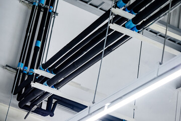 Black plumbing pipes installed with long white LED light lamp hanging on the ceiling in warehouse or factory. Piping equipment for water system in the industrial building