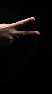 Rock paper scissors game on black background.
Man showing scissors in game.
Male hand imitating scissors in dark room