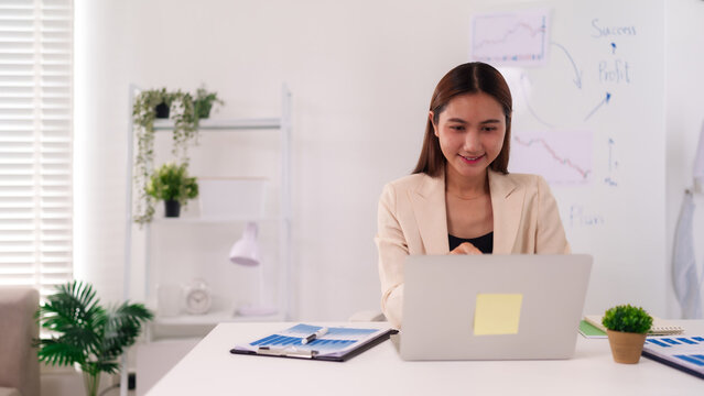 Asian adult businesswoman uses laptop for remote work analyzing financial data achieving profit growth at modern home office