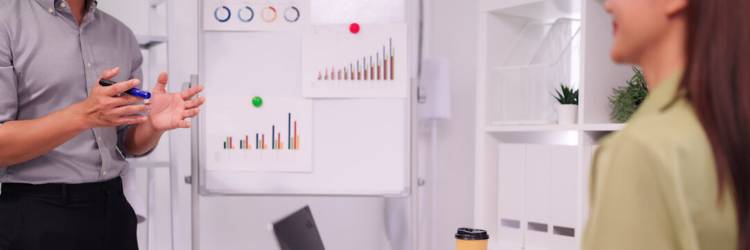 Asian adult man presenting business strategy data charts on whiteboard during office meeting to Asian adult woman - Powered by Adobe