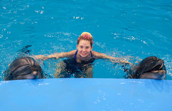 Woman interacts with dolphins in a blue pool during a marine park encounter