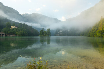 Naklejka premium Mystischer Morgen am Königssee in Schönau mit Bootshäusern und Christlieger. Sonnenaufgang und schöne Nebelschwaden über dem Königssee im Kessel.