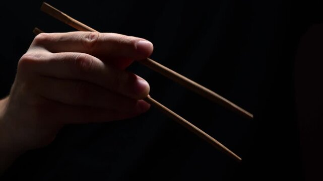 Using Japanese or Chinese chopsticks in a restaurant on a black background.
Bamboo chopsticks in Asian culture.
Ancient Asian food traditions and eating culture
