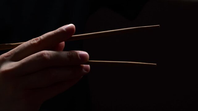 chopsticks on a black background in the hands of an Asian man.
Chopsticks for sushi and sashimi are used.
Japanese traditional chopsticks large stick in the hands of a man