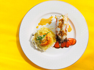 Baked Lobster Tail and Scallop with Linguine Pasta and Lemon Cream Sauce served in plate top view of luxurious meal