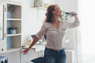 Middle-aged woman at home enjoying leisure time, using smartphone, dancing, surrounded by plants, smiling and relaxed, independent lifestyle, having fun, personal freedom, carefree and joyful moments