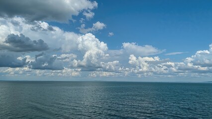 A serene lake under an overcast sky with diverse cloud formations casting reflections on the deep blue surface.