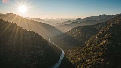 Obraz premium Magnificent highland vista showing ridge silhouettes bathed in early morning sunlight, soft mist enveloping a deep ravine with a flowing river and winding road, wide valley panorama during summer.