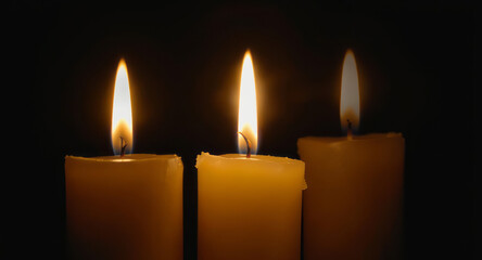 Three lit candle flame glowing in dark background with warm light creating calm and peaceful atmosphere