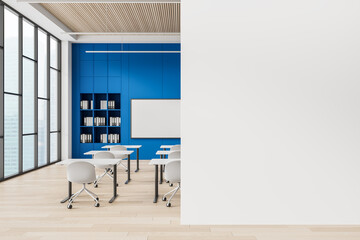 Modern classroom interior with blue wall, desks, white chairs, and a blank vertical poster mockup on clean wall for branding or design presentation. 3D Rendering
