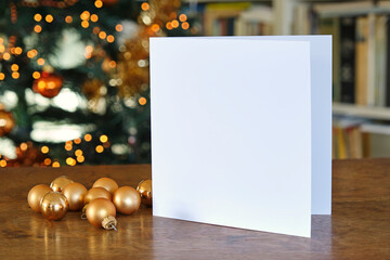 Standing blank empty square greeting card mock up with Christmas balls and before a blurred christmas tree with copy space. For use as a Christmas background template.	