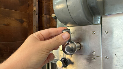 A hand delicately adjusts a vintage coffee roaster, evoking aromatic landscapes, perfect for...
