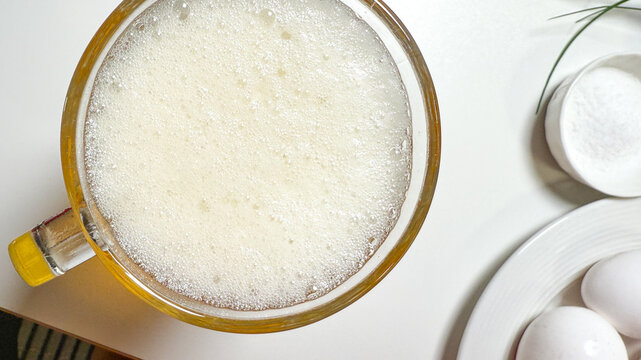 Frothy milk foams in a cozy mug beside eggs, highlighting brunch tranquility and World Egg Day celebrations