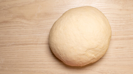 Puffy dough ball on rustic wooden table, evoking anticipation of Lammas loaf baking, celebrating yeast alchemy and cozy warmth