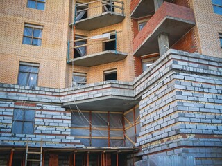 Fototapeta premium A multi-story building under construction with brickwork and balconies, outdoors in daylight.