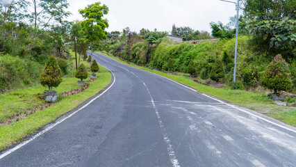 Uphill road curves through a vibrant green landscape with lush vegetation and a cloudy sky