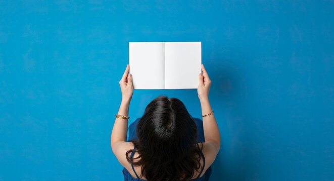 Overhead shot of a woman holding open a blank book against a blue background