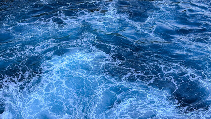 Blue sea water texture with frothy waves. White foam texture background with turquoise and blue colors, perfect for natural backgrounds and ocean themed designs.
