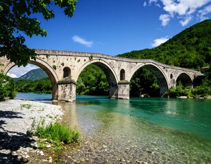Fototapeta premium Stone arch bridge over a clear river, with lush green surroundings