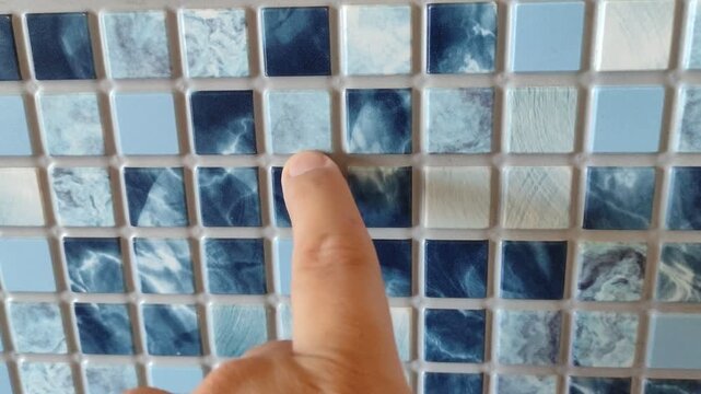 Man touches a tile on a wall with his finger