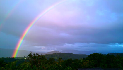 Naklejka premium Vibrant Double Rainbow Arches Across a Moody, Lavender-Hued Sky Over Lush Mountains