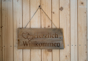 Willkommensschild mit Herzmotiv auf Holz vor einer Holzwand als rustikale Deko für Haus Eingang...