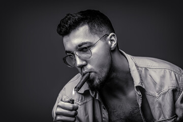 Male smoking a lit cigar, with smoke swirling around, capturing the burning. Man in glasses and...