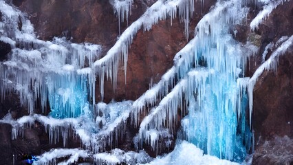 Winter waterfall cascades over icy rocks and stones, its frozen icicles clinging to the frigid mountain landscape