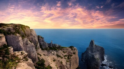 Golden light bathes the coastal landscape, where the setting sun dips below the horizon, casting vibrant colors across the ocean and sky