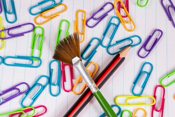 Clips fluorescentes de colores un pincel y un lápiz sobre una hoja de rallas azules