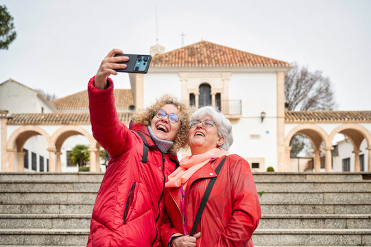 Two mature women smiling while taking a selfie together during sightseeing trip, enjoying travel moments and digital memories in front of historical building