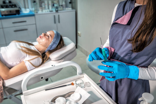 Professional cosmetologist in blue medical gloves dials a rejuvenating medicine from an ampoule into a syringe.