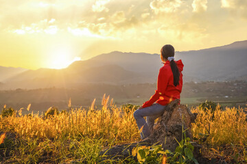 Fototapeta premium Cheerful young girl sitting on the field at sunset