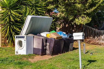 Hard rubbish left on the front yard garden of a suburban property featuring an old washing machine,...