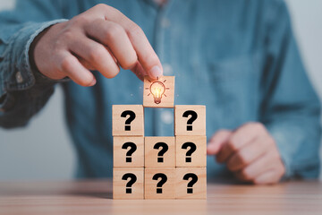 Hand putting wooden cube block stacking which print screen glowing light bulb and question mark for Creative thinking idea and problem solving concept.