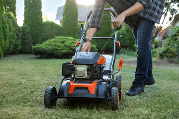 Man pulling starter cord of lawn mower in garden, closeup