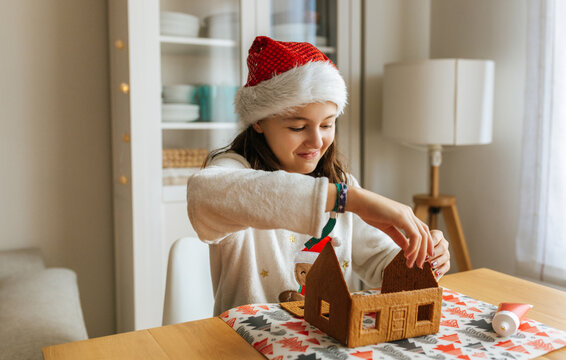 Smiling girl assembling gingerbread house for Christmas holiday tradition
