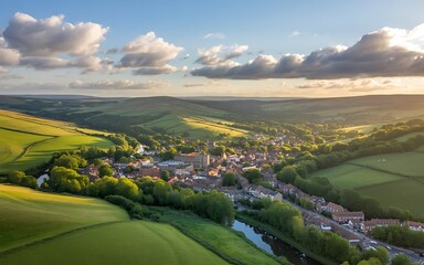 Aerial view of a picturesque English village nestled in rolling green hills at sunset with dramatic clouds Keywords: aerial, village, town, countryside, England, UK, British, rural, landscape
