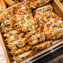 Freshly baked bread rolls filled with sausage and herbs displayed in a wooden basket at a local bakery in the afternoon