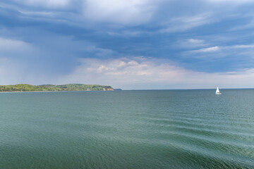 The coast of the Baltic Sea in northern Poland. Sailboat glides on expansive ocean waters under a dramatic sky, serene landscape.