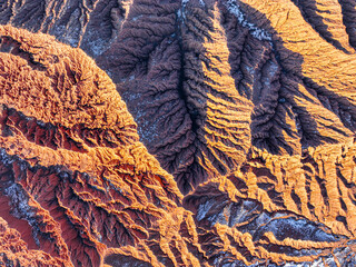 A close up, abstract aerial shot highlights the intricate, jagged patterns and textures of the red rock formations in Mars Canyon with light snow
