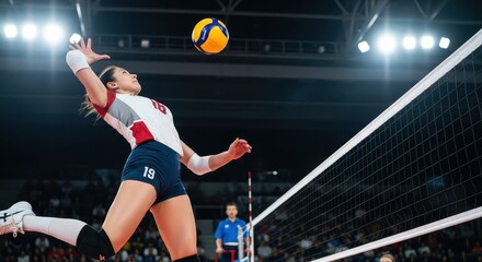 A powerful female volleyball player in mid-air, spiking the ball hard over the net in a stadium.