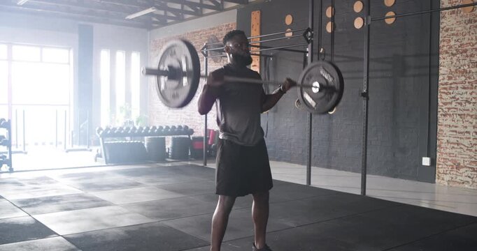 From front rack, athlete is driving through legs and pressing barbell overhead in gym for strength