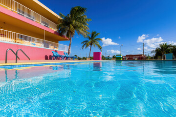 Fototapeta premium Vibrant swimming pool scene with clear blue water, palm trees, and colorful building in background creates relaxing atmosphere