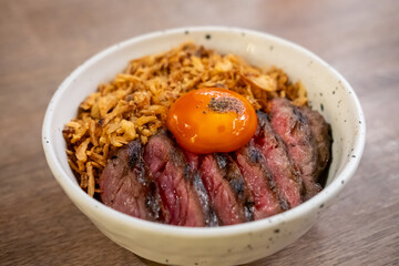A bowl of Medium rare striploin steak, fried garlic with pickled egg yolk on top.