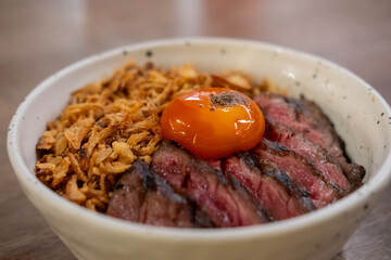 A bowl of Medium rare striploin steak, fried garlic with pickled egg yolk on top.