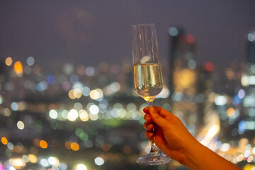 A hand holding a glass of Prosecco or sparkling wine with colorful sunset sky and city view on the background